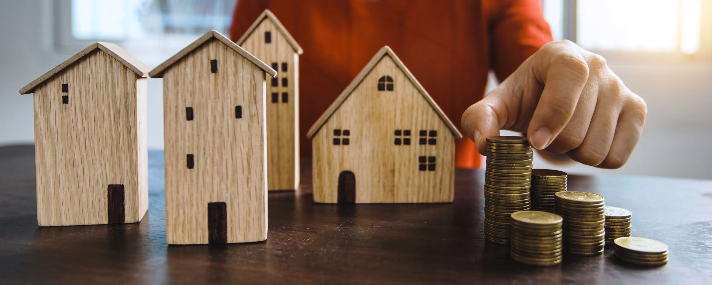 Wooden model houses beside a rising stack of coins